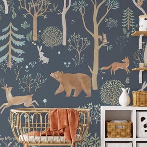 May include: A blue and brown woodland nursery wallpaper featuring a bear, deer, fox, and rabbit. The wallpaper is decorated with trees, flowers, and leaves. The wallpaper is shown in a nursery setting with a cot, shelves, and baskets.