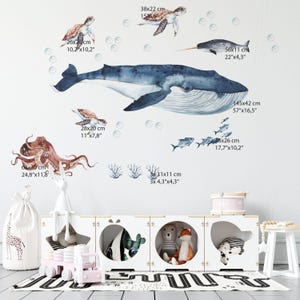 May include: A set of wall decals featuring a large blue whale, a brown octopus, two sea turtles, a narwhal, small fish, and coral. The decals include printed dimensions in cm, such as the whale at 145x42 cm and the octopus at 63x30 cm.