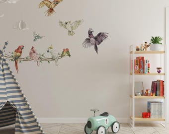 Pode incluir: Um conjunto de autocolantes de parede com ilustrações em aguarela de várias aves, incluindo uma arara grande a voar, uma cacatua branca, uma cacatua cinzenta escura e várias aves pequenas pousadas num ramo, aplicados numa parede lisa.
