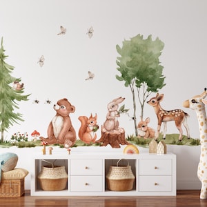May include: A wall decal set featuring watercolor illustrations of a brown bear, a squirrel, a rabbit, a deer, and a fawn in a forest setting with green trees, mushrooms, and butterflies. The scene includes a tall pine tree and a deciduous tree.