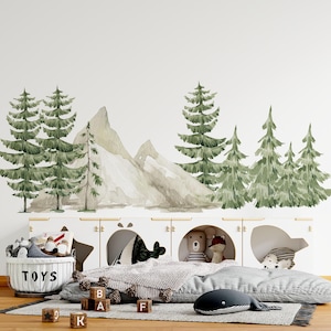 Può includere: Un set di adesivi murali con pini verdi e montagne beige in stile acquerello. Il design include diversi alberi sempreverdi di varie altezze disposti attorno a due cime montuose, creando un paesaggio boschivo per decorare le pareti.