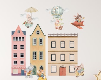 May include: A wall decal set featuring three multi-story buildings in pink, yellow, and beige, accompanied by illustrations of animals including rabbits, an elephant, and a fox traveling by bicycle, scooter, airplane, and hot air balloon.