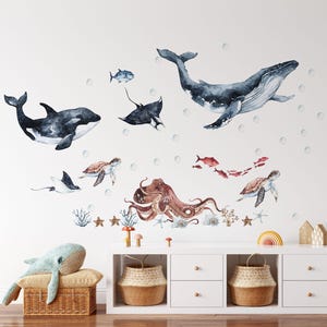 Könnte beinhalten: Ein Set aus Aquarell-Wandaufklebern mit einem großen Blauwal, einem Orca, zwei Meeresschildkröten, einem Oktopus, einem Mantarochen und kleineren Fischen. Die Meeresmotive sind mit verstreuten Blasen, Korallen und Seesternen arrangiert.