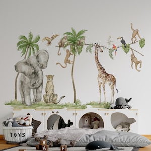 May include: A nursery wall decal set featuring a jungle theme with a gray elephant, a cheetah, a giraffe, monkeys, toucans, and palm trees. The decals are on a white wall with a white shelf and a gray blanket on the floor.