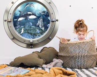 May include: A circular wall decal featuring a metallic porthole frame surrounding an underwater scene with an orca, dolphins, and jellyfish. The design displays various marine life in shades of blue and white, creating a realistic ocean view.