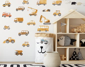 May include: A collection of watercolor-style wall decals featuring various construction vehicles, trucks, and cars in shades of yellow and orange, arranged on a wall above a wooden toy shelf, a fabric storage bin, and a black and white road rug.