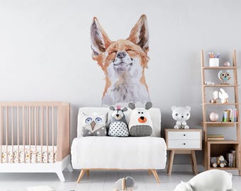 May include: A large wall decal featuring a watercolor-style illustration of a fox with its eyes closed and a smiling expression. The fox is rendered in shades of orange, brown, and white, positioned above a white sofa with three animal-shaped pillows.