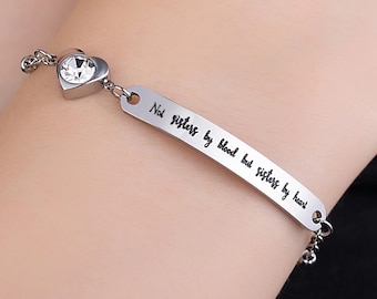 May include: Silver bracelet with a heart charm and a small crystal. The bracelet has an inscription that reads "Not sisters by blood but sisters by heart."