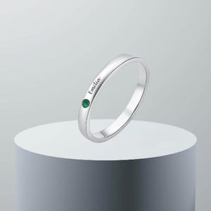 Könnte beinhalten: Ein silberner Ring mit der Gravur "Emilia" auf der Band und einem kleinen grünen Edelstein.