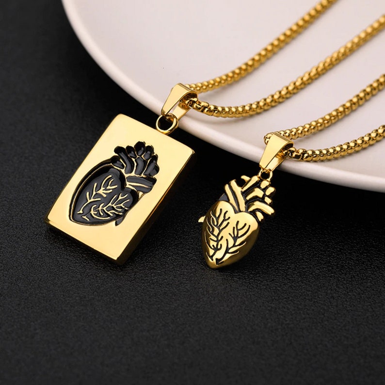 Pu&ograve; includere: Due collane d'oro con ciondoli a forma di cuore anatomico. Un ciondolo &egrave; un ritaglio rettangolare con un cuore nero all'interno. L'altro ciondolo &egrave; un cuore pieno.