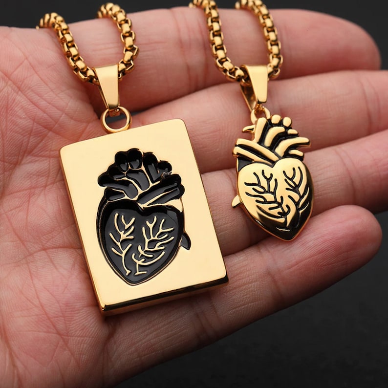 Pu&ograve; includere: Due collane d'oro con ciondoli a forma di cuore anatomico. Un ciondolo &egrave; una cornice rettangolare con un cuore nero all'interno. L'altro ciondolo &egrave; un cuore tridimensionale.