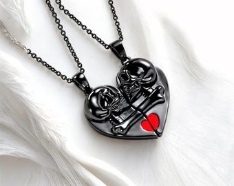 Può includere: Due collane in metallo nero con un ciondolo a forma di cuore che presenta due teschi con ossa incrociate e un cuore rosso. Le collane sono intrecciate e il ciondolo è diviso in due.