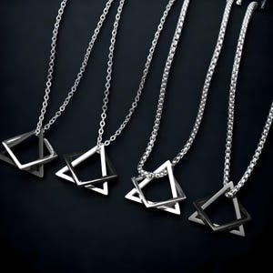 May include: Four silver necklaces with geometric pendant charms. Each pendant features a silver triangle with a smaller silver square inside. The necklaces are on a black background.