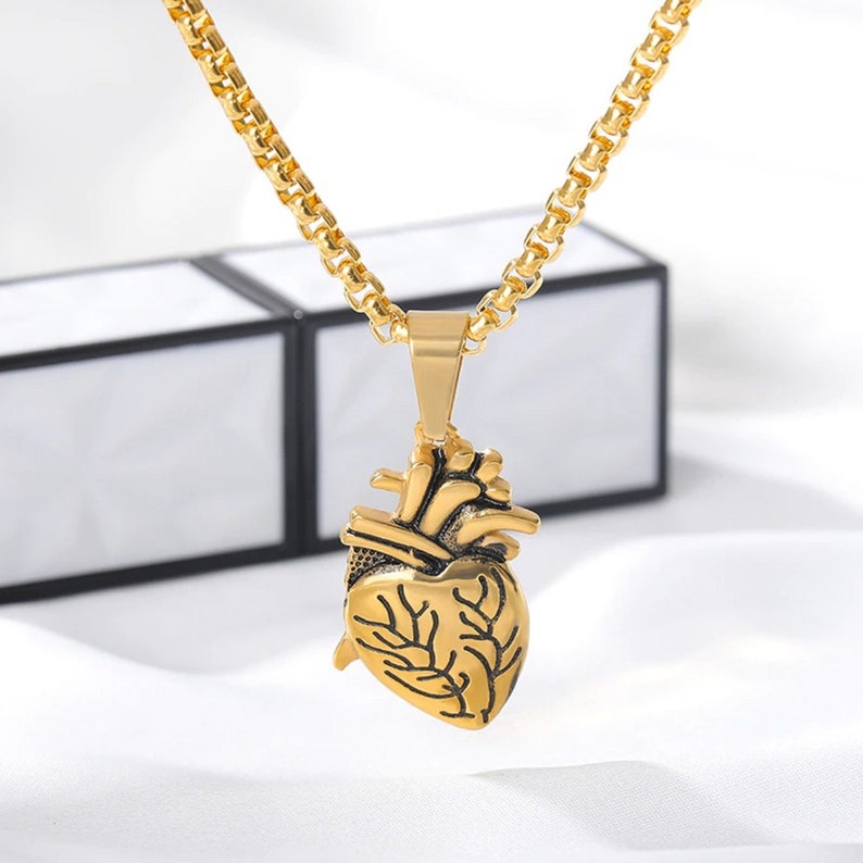 Pu&ograve; includere: Una collana con catena dorata con un ciondolo a forma di cuore anatomico dettagliato.