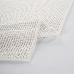 May include: A white, textured bath mat with a raised, bubble-like pattern on one section and a ribbed design on another. The mat is folded over, showcasing the different textures and the clean, white color.