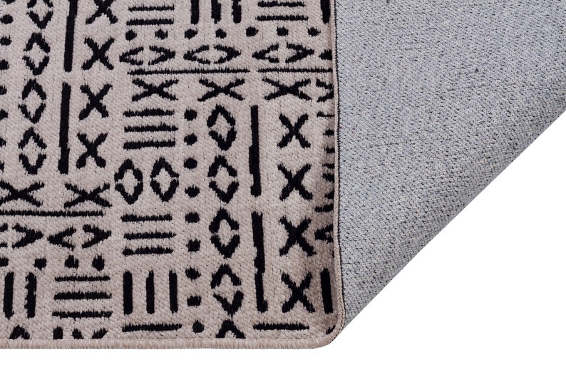 May include: A beige rug with a black geometric pattern. The rug has a gray backing.