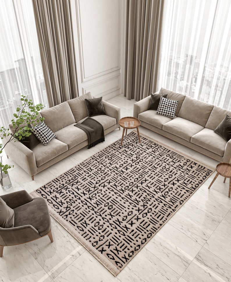 May include: A beige and black patterned rug with a geometric design. The rug is laid out on a light gray tiled floor in a living room setting with two beige sofas and a wooden side table.