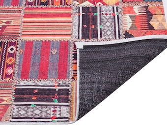 May include: A colorful patchwork rug with a variety of geometric patterns in shades of red, orange, yellow, blue, and black. The rug has a fringed edge and a black backing.