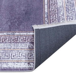 May include: A purple and white area rug with a geometric pattern. The rug has a fringe border and a gray backing.