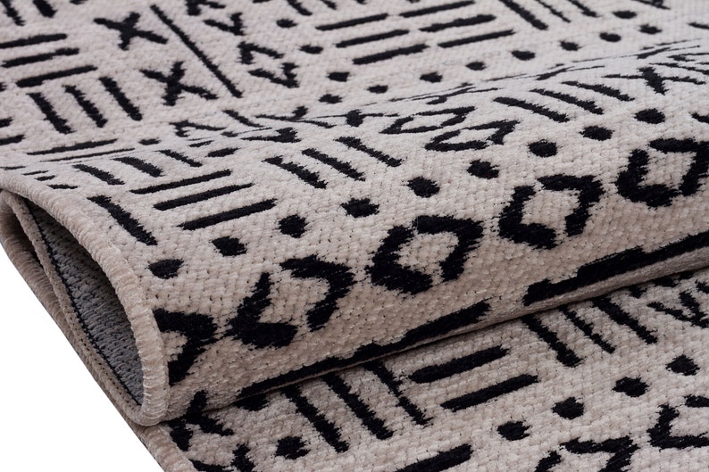 May include: Close-up of a beige and black patterned rug with a geometric design. The rug has a fringe border.