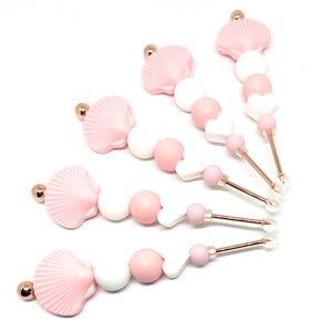 May include: Five pink and white silicone teething toys with a seashell and heart design. Each toy has a gold-colored metal rod and a clear plastic tip.