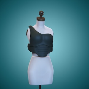 May include: A dark green, one-shoulder, padded, and segmented chest piece on a white mannequin.