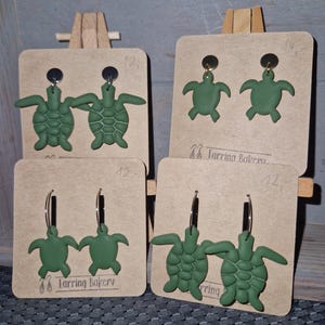 Op de afbeelding: Vier paar groene schildpad oorbellen gepresenteerd op bruine kartonnen oorbellenkaarten. Twee paar zijn oorstekers en twee paar zijn oorringen. De tekst "Earring Bakery" staat op de kaarten.