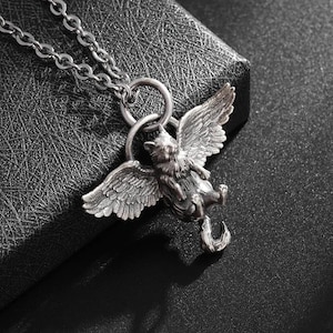 May include: A silver-colored pendant necklace featuring a winged cat design. The cat has detailed wings and is suspended from a chain. The pendant is intricately detailed and has a vintage aesthetic.