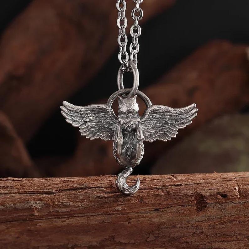 May include: A silver-toned pendant necklace featuring a detailed winged fox design. The fox has outstretched wings and a curled tail. The pendant hangs from a delicate chain, creating a striking piece of jewelry.