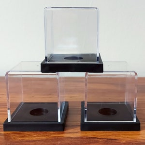 May include: Three clear acrylic display cases with black bases. The cases are stacked on top of each other.