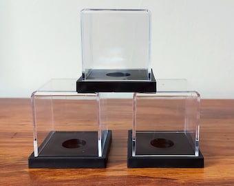May include: Three clear acrylic display cases with black bases. The cases are stacked on top of each other.