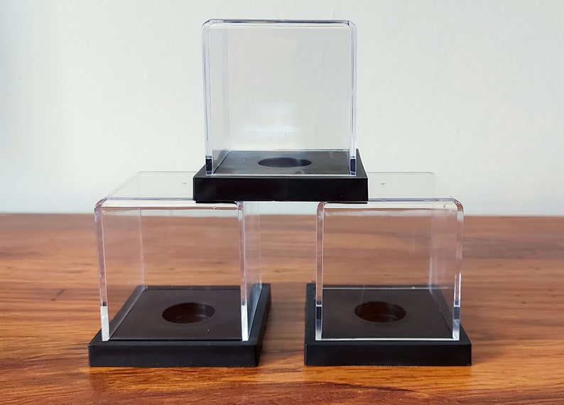 May include: Three clear acrylic display cases with black bases. The cases are stacked on top of each other.