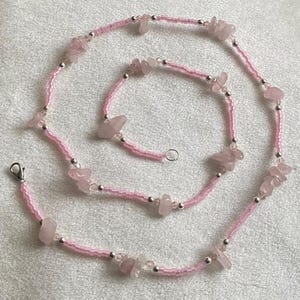Puede incluir: Un collar de cuentas rosadas con piedras de cuarzo rosa. El collar est&aacute; hecho de peque&ntilde;as cuentas rosadas y tiene un cierre plateado.