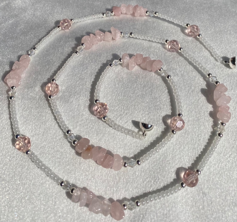 May include: A long necklace made with white beads, pink rose quartz chips, and pink faceted beads. The necklace has a silver clasp.