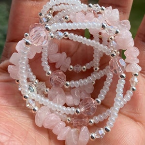 May include: A multi-strand bracelet featuring pink and white beads. The bracelet is made with small, round white beads, larger pink and clear faceted beads, and larger, irregular shaped pink beads.