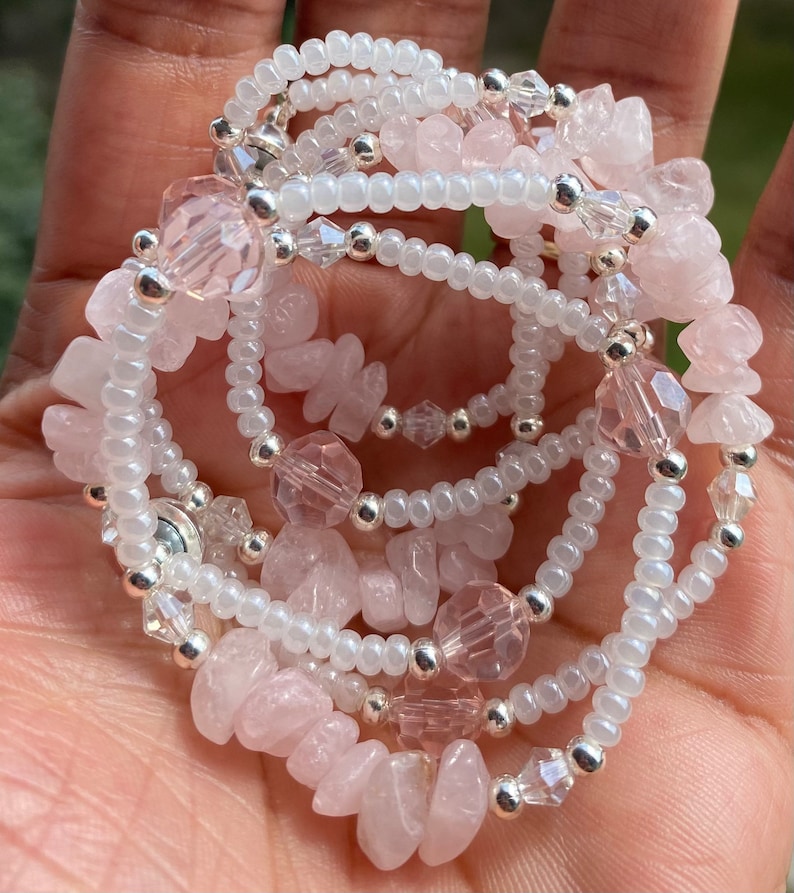 May include: A multi-strand bracelet featuring pink and white beads. The bracelet is made with small, round white beads, larger pink and clear faceted beads, and larger, irregular shaped pink beads.