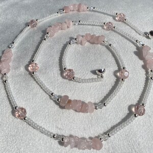 May include: A long, delicate necklace made with white beads and pink rose quartz stones. The necklace has a silver clasp.