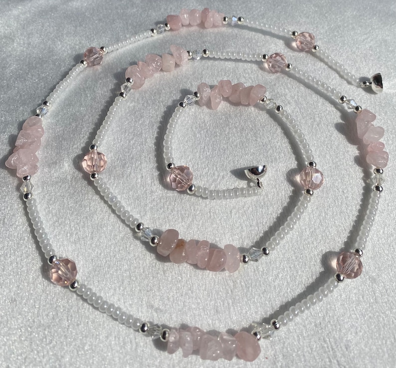 May include: A long, delicate necklace made with white beads and pink rose quartz stones. The necklace has a silver clasp.