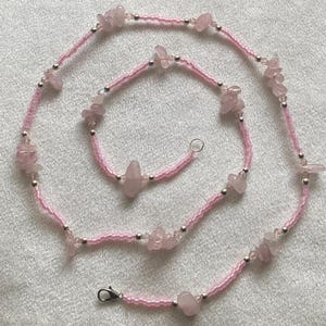 Puede incluir: Un collar de cuentas rosadas y plateadas con piedras de cuarzo rosa. El collar est&aacute; hecho de cuentas peque&ntilde;as y tiene un aspecto delicado.