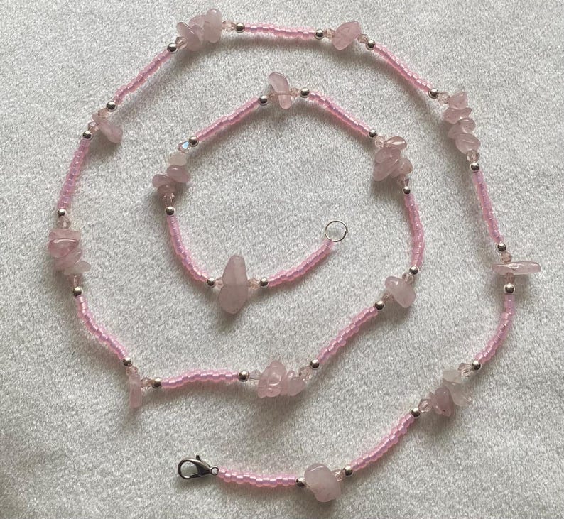 Puede incluir: Un collar de cuentas rosadas y plateadas con piedras de cuarzo rosa. El collar est&aacute; hecho de cuentas peque&ntilde;as y tiene un aspecto delicado.