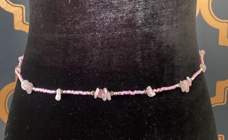 Puede incluir: Una cadena de cintura de cuentas rosadas y plateadas con detalles de piedras rosadas.