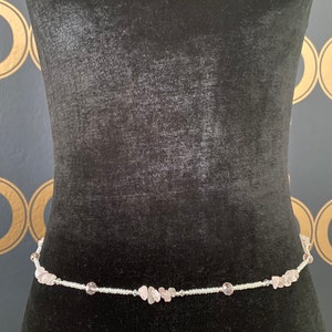 May include: A delicate waist chain made of small white beads and light pink gemstone accents.