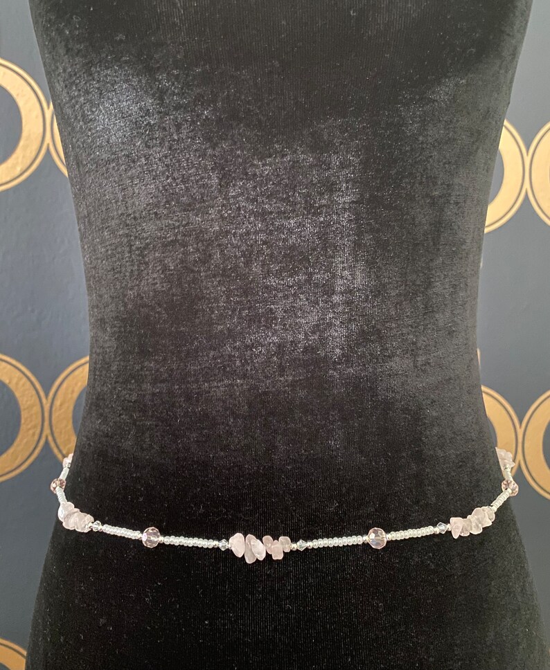 May include: A delicate waist chain made of small white beads and light pink gemstone accents.
