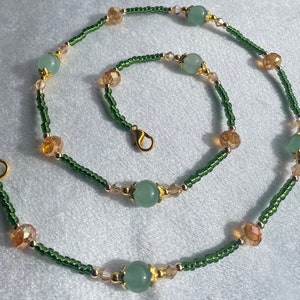 May include: A green and gold beaded necklace with a clasp closure. The necklace features alternating green and gold beads, with larger green beads spaced throughout.