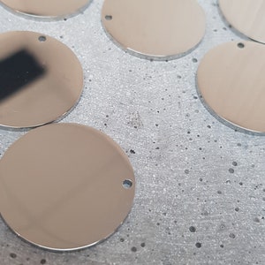May include: A group of eight silver round metal tags with a hole in the center. The tags are arranged in a semi-circle on a textured surface.