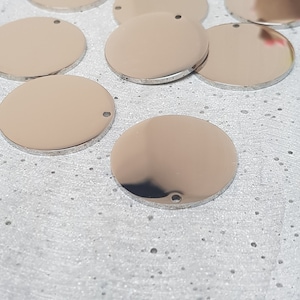 May include: A group of eight silver-colored metal circles with a small hole in the center. The circles are arranged in a semi-circle on a white textured surface.