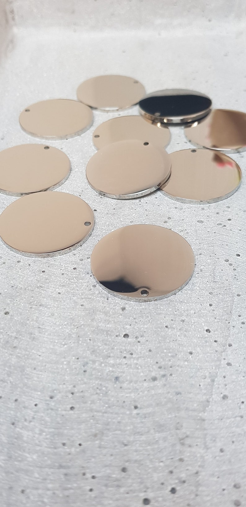 May include: A group of eight silver-colored metal circles with a small hole in the center. The circles are arranged in a semi-circle on a white textured surface.