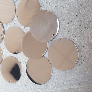 May include: A group of ten silver-colored metal circles with a hole in the center. The circles are arranged in a semi-circle on a white surface.