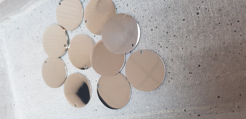 May include: A group of ten silver-colored metal circles with a hole in the center. The circles are arranged in a semi-circle on a white surface.