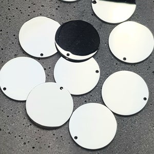 May include: A collection of nine silver-colored metal circles with a hole in the center. The circles are arranged in a random pattern on a gray textured surface.
